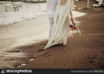 Bride groom walking on choppy Beach, bride has flowers in her hand