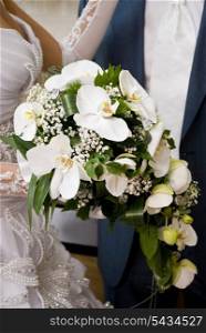 Bride hold the bouquet from orchids and stand near the groom
