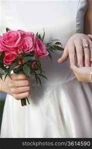 Bride holding bouquet and touching groom&acute;s hand, mid-section, close-up of hands