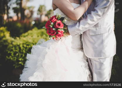 Bride holds a wedding red rose bouquet in hands, the groom hugs . Bride holds a wedding red rose bouquet in hands, the groom hugs his bride together. Wedding lover concept.