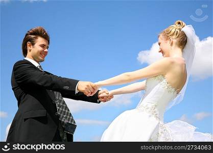 bride holds fiance for the hands against the background of the sky