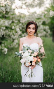 bride in a white dress with a large spring bouquet in a green forest