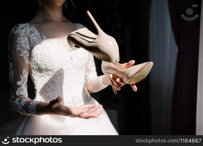 Bride in a white wedding dress holding wedding shoes. Bride in a white wedding dress holding wedding shoes in her hands