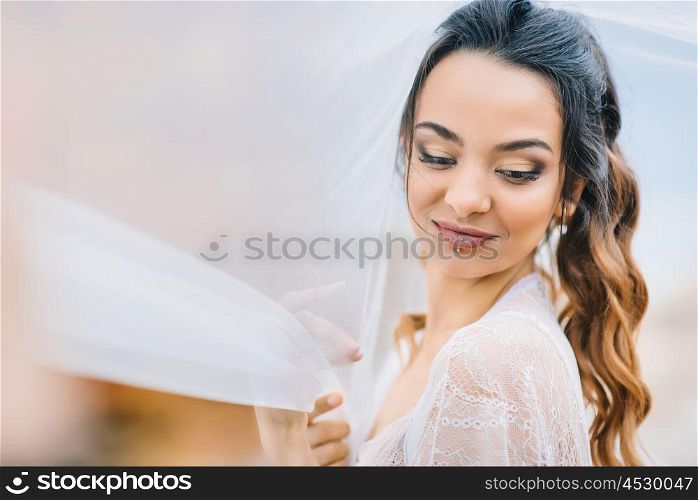 bride in her underwear and a dressing gown with a veil walks on the beach