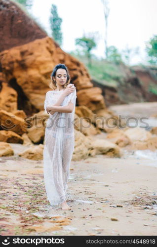 bride in her underwear and a dressing gown with a veil walks on the beach