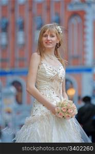 Bride in light dress with cream-colour rose bouquet in her hands and white flowers in her hair.