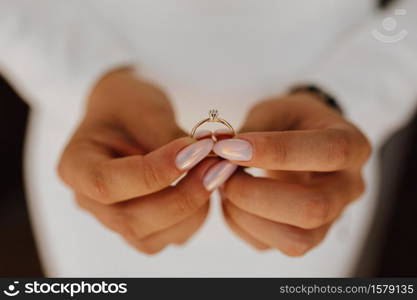 Bride is holding engagement ring with diamond in hands with beautiful manicure, front view, wedding day