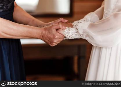 Bride on wedding day holding her mother's hands. Concept of relationship between moms and daughters. an old woman holds her young daughter married. Bride on wedding day holding her mother's hands. an old woman holds her young daughter married. Concept of relationship between moms and daughters