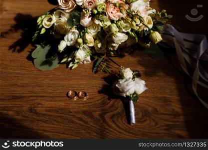 bride&rsquo;s bouquet, groom&rsquo;s boutonniere and gold wedding rings on a wooden rustic table. wedding accessories. selective focus.. bride&rsquo;s bouquet, groom&rsquo;s boutonniere and gold wedding rings on a wooden rustic table. wedding accessories. selective focus