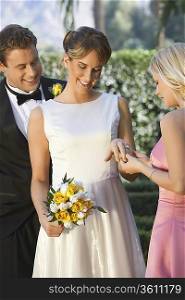 Bride showing ring to bridesmaid, groom looking on