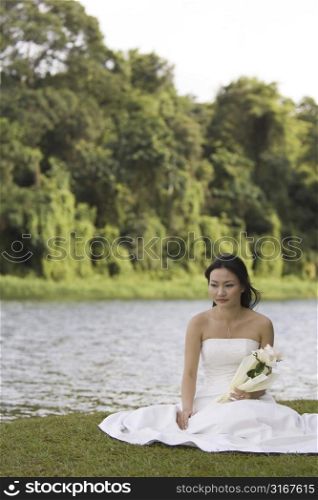 Bride sitting at the lakeside and holding a bouquet of flowers