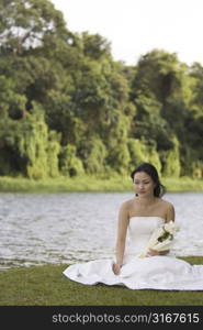 Bride sitting at the lakeside and holding a bouquet of flowers