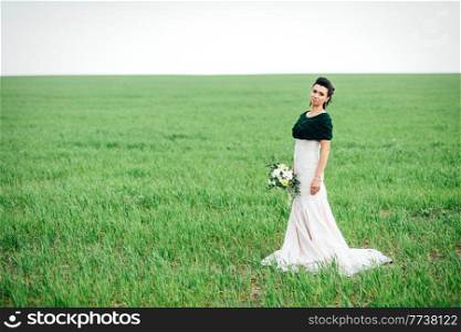 bride with a bouquet in an ivory dress and a knitted shawl on a green field