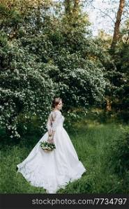 bride with a wedding bouquet in the forest near the bushes blooming with white flowers