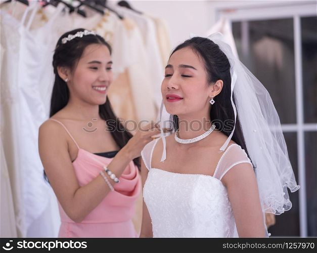 Bridesmaid helping bride adjusting dress on the wedding day in the dressing room.