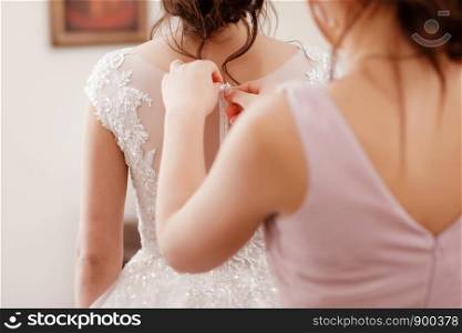 Bridesmaid helping bride fasten corset and getting her dress, preparing bride in morning for the wedding day. bride's meeting. Bridesmaid helping bride fasten corset and getting her dress, preparing bride in morning for the wedding day. bride's meeting.