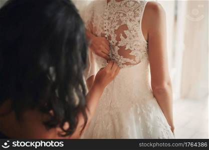 Bridesmaid helping bride fasten corset close-up and getting her dress, preparation concept in morning for wedding ceremony. Bridesmaid helping bride fasten corset close-up and getting her dress, preparation concept in morning for wedding ceremony.