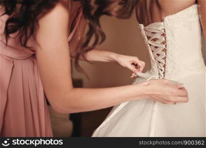 Bridesmaid helping bride fasten corset close-up and getting her dress, preparation concept in morning for wedding ceremony.. Bridesmaid helping bride fasten corset close-up and getting her dress, preparation concept in morning for wedding day.