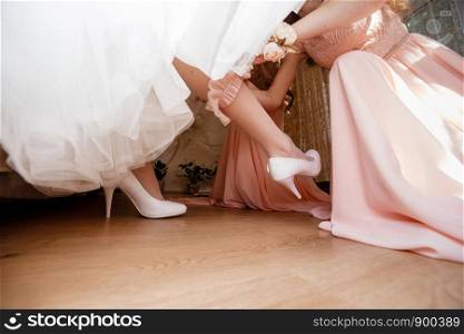 Bridesmaid preparing bride for wedding day. the Bridesmaid helps her to wear. Bridesmaid preparing bride for wedding day. the Bridesmaid helps her to wear a dressing-jewelry on her leg. Wedding morning moments details concept