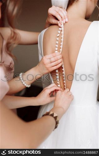 Bridesmaid&rsquo;s hands helping bride fastens with buttons on the back of a beautiful white wedding lace vintage dress close-up, preparation concept in morning for wedding day.. Bridesmaid&rsquo;s hands helping bride fastens with buttons on the back of a beautiful white wedding lace vintage dress close-up, preparation concept in morning for wedding day