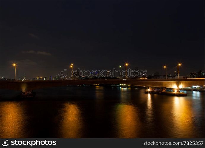 Bridge across the river at night with lights of cars that run on electricity and a bridge. Ships in the river.