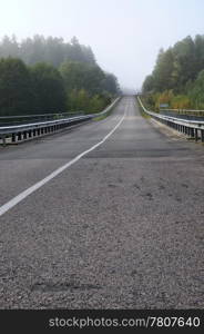 Bridge and countryside road. Forest in a mist. Early autumn morning