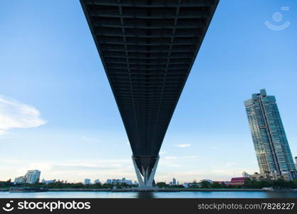 Bridge over a large river. Of surface reflects blue sky. Opposite side of the building in the city.