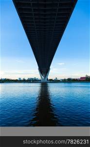 Bridge over a large river. Of surface reflects blue sky. Opposite side of the building in the city.