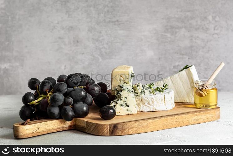 Brie, camembert, and roquefort on a wooden board. Food for wine, party and romantic dinner, cheese delicatessen with grapes and honey.