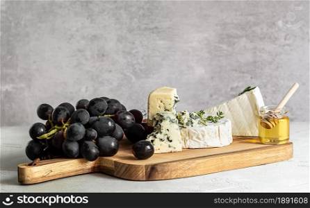 Brie, camembert, and roquefort on a wooden board. Food for wine, party and romantic dinner, cheese delicatessen with grapes and honey.