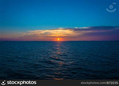 Bright beautiful sunset at the White sea with dark blue water and purple-orange clouds.