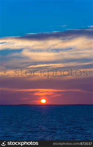 Bright beautiful sunset at the White sea with dark blue water and purple-orange clouds.