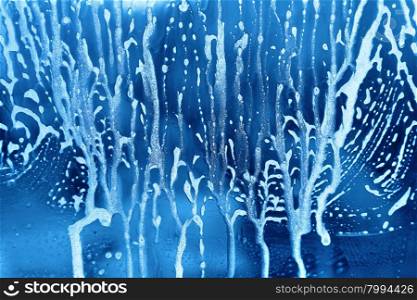 Bright blue abstract texture with soap foam on glass