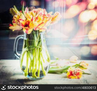 Bright bouquet of tulips in glass jug on table at sunny spring day background with bokeh, front view