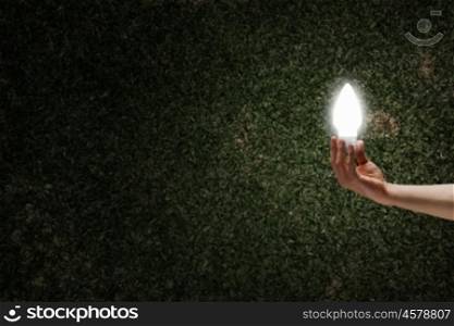 Bright bulb in darkness. Male hand on dark background showing glass light bulb