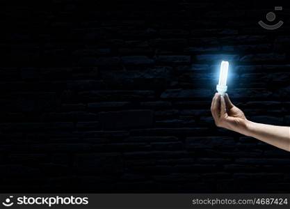 Bright bulb in darkness. Male hand on dark background showing glass light bulb