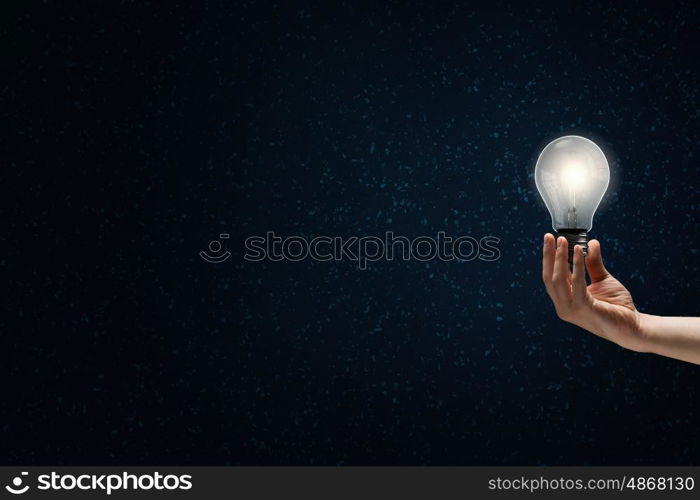 Bright bulb in darkness. Male hand on dark background showing glass light bulb