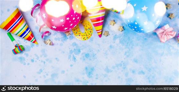 Bright colorful carnival or party scene. Bright colorful carnival or party border of balloons, streamers and confetti on blue table. Flat lay style, birthday or party greeting card with copy space and bokeh lights