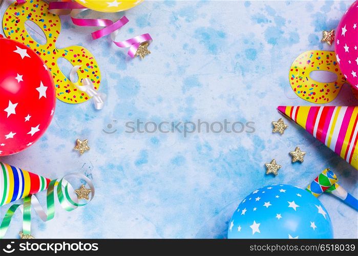 Bright colorful carnival or party scene. Bright colorful carnival or party border of balloons, streamers and confetti on blue table background. Flat lay style, birthday or festive party greeting card with copy space.