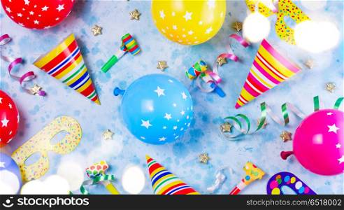 Bright colorful carnival or party scene. Bright colorful carnival or party pattern of balloons, streamers and confetti on blue table. Flat lay style, birthday or party greeting card and bokeh lights