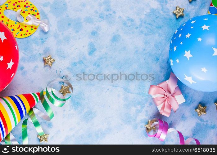 Bright colorful carnival or party scene. Bright colorful carnival or party scene of balloons, streamers and confetti on blue table. Flat lay style, birthday or carnival party greeting card with copy space.