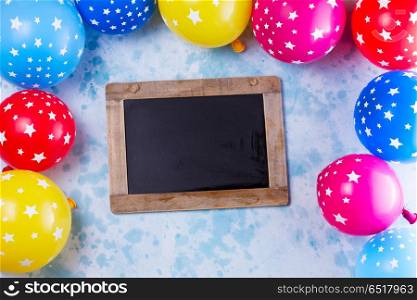 Bright colorful carnival or party scene. colorful carnival or party scene frame of balloons on blue table. Flat lay style frame, birthday or party greeting card with copy space on blackboard.
