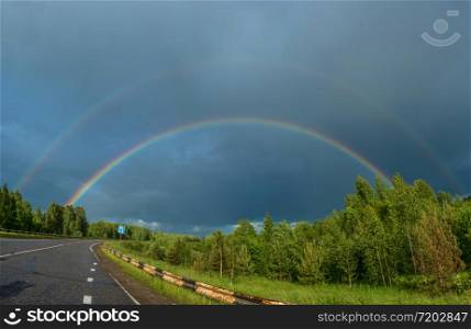 Bright colorful rainbow over the highway on the background of the cloudy sky.