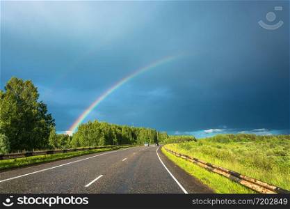 Bright colorful rainbow over the highway on the background of the cloudy sky.