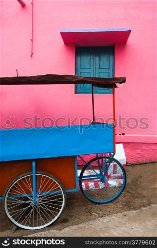 Bright colors of Indian street life. Colorful composition of empty blue vendor cart near pink painted wall with window. South India, Tamil Nadu