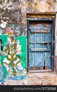 Bright colors of Indian street life. Colorful composition with old blue door and cracked religious painting on grunge wall. South India, Tamil Nadu