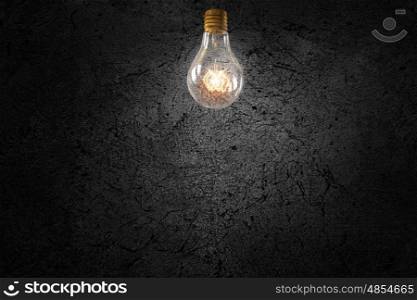 Bright electric bulb. Glowing glass light bulb on concrete background
