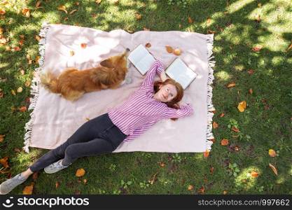 bright fun autumn. girl and dog Corgi lie on a plaid on the lawn and read books