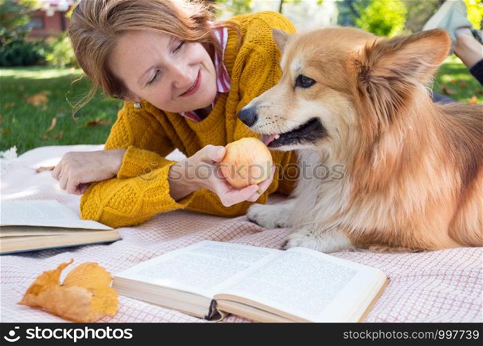 bright fun autumn. girl and dog Corgi lie on a plaid on the lawn and read books