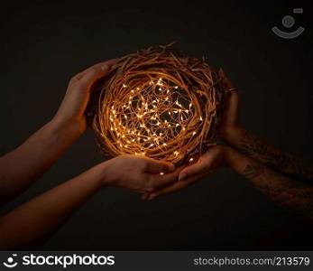 Bright garlands. decorating a wreath of branches in the hands of a woman with a tattoo and men on the black background. Christmas concept. Christmas wreath of branches with yellow garlands. hold hands of man and woman with tattoo around dark background